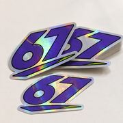 Sample mockup of purple 67 holographic vinyl stickers with rainbow reflections and a small stack.