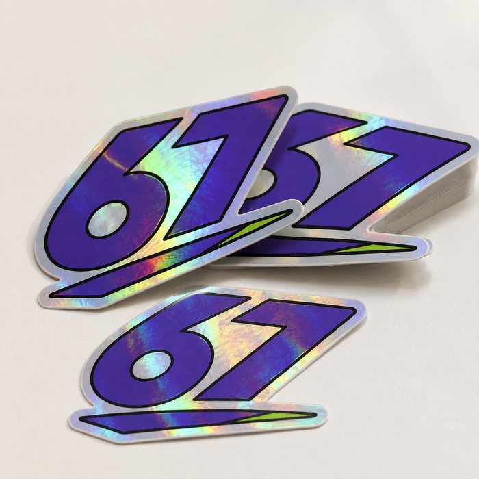 Sample mockup of purple 67 holographic vinyl stickers with rainbow reflections and a small stack.
